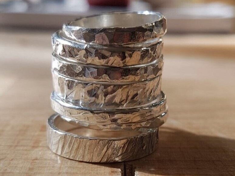 A stack of handmade silver rings on a wooden table